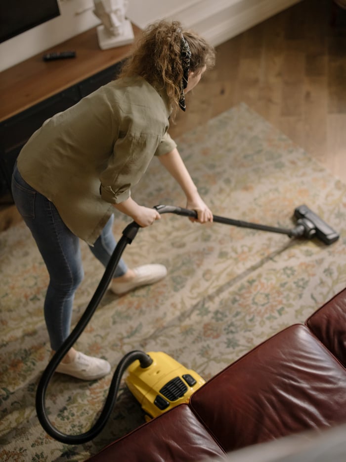 services-02 High-angle view of a woman vacuuming a patterned carpet in a stylish living room.