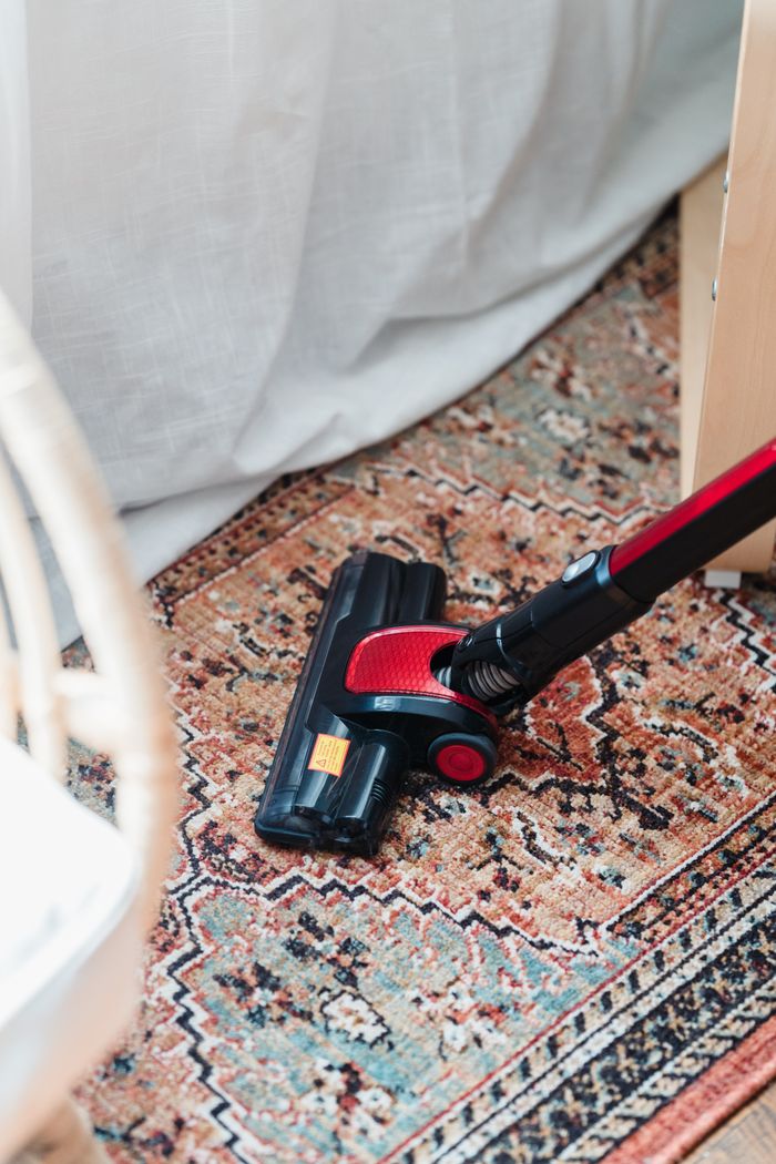 services-03 A red and black vacuum cleaner on a vibrant patterned carpet indoors, showcasing home cleaning essentials.