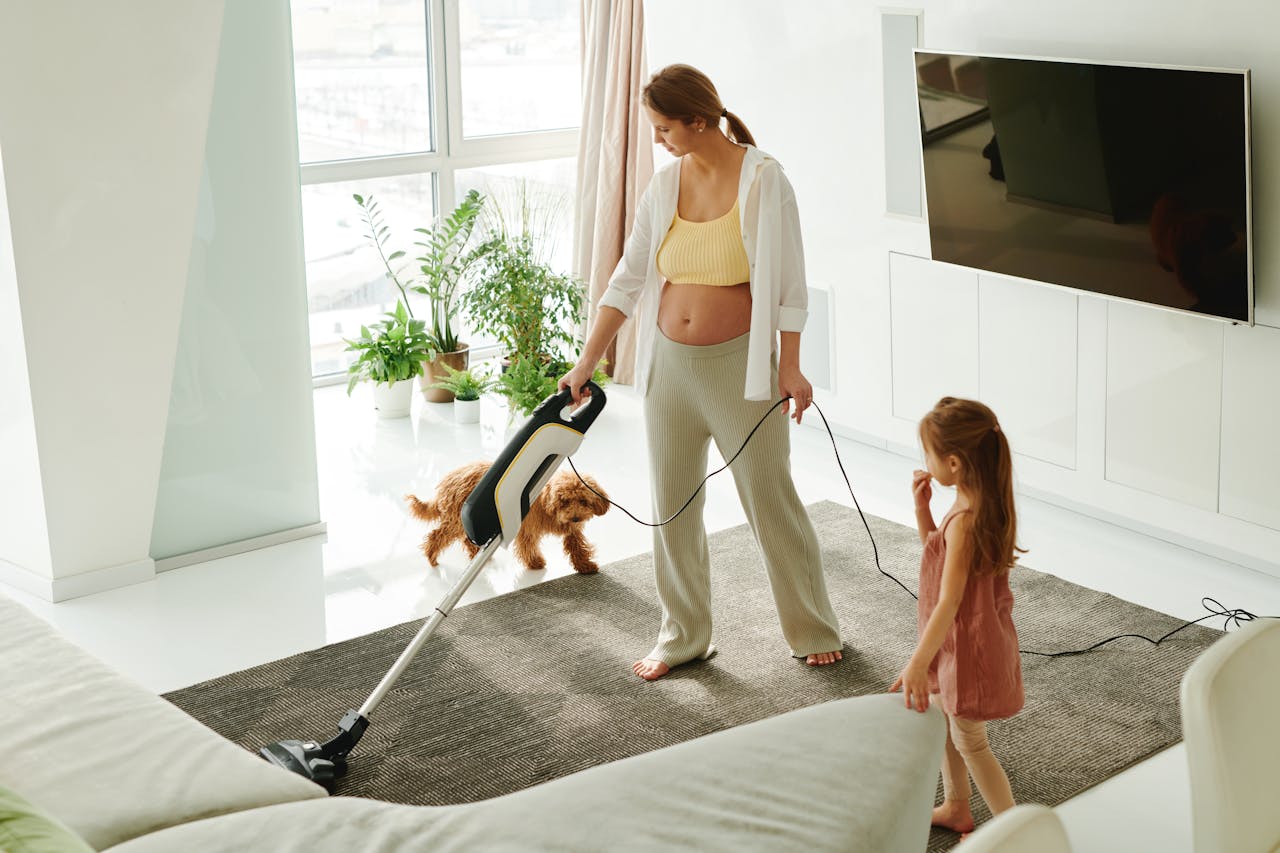 why-choose-us Pregnant mother cleaning carpet with vacuum as daughter and dog play indoors.