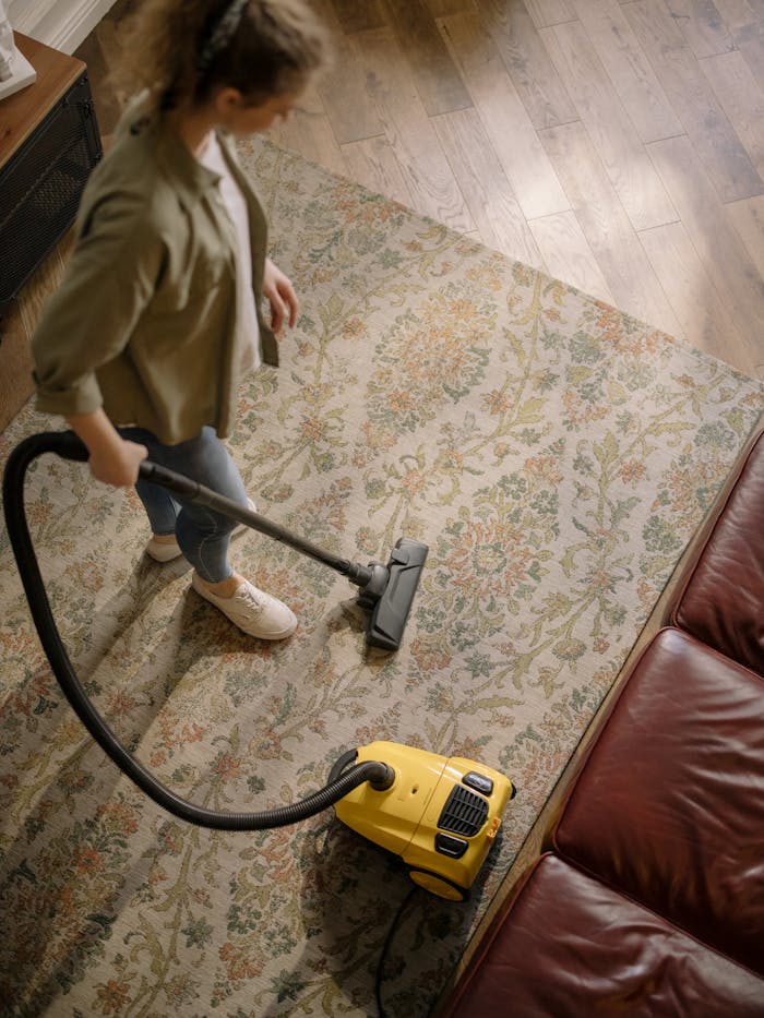 about-01 Overhead view of a woman vacuuming a carpet at home, highlighting cleanliness and housekeeping.